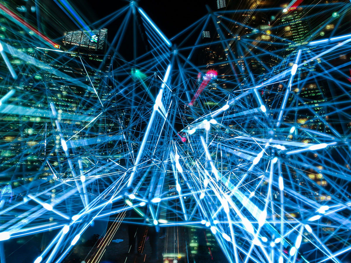 Image from: https://www.pexels.com/photo/time-lapse-photography-of-blue-lights-373543/ Network of light beams in front of city buildings at night